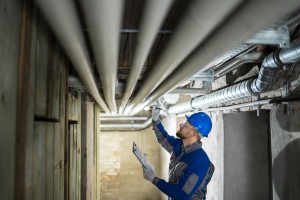 Male Worker Inspecting Water Pipes For Leaks In Basement